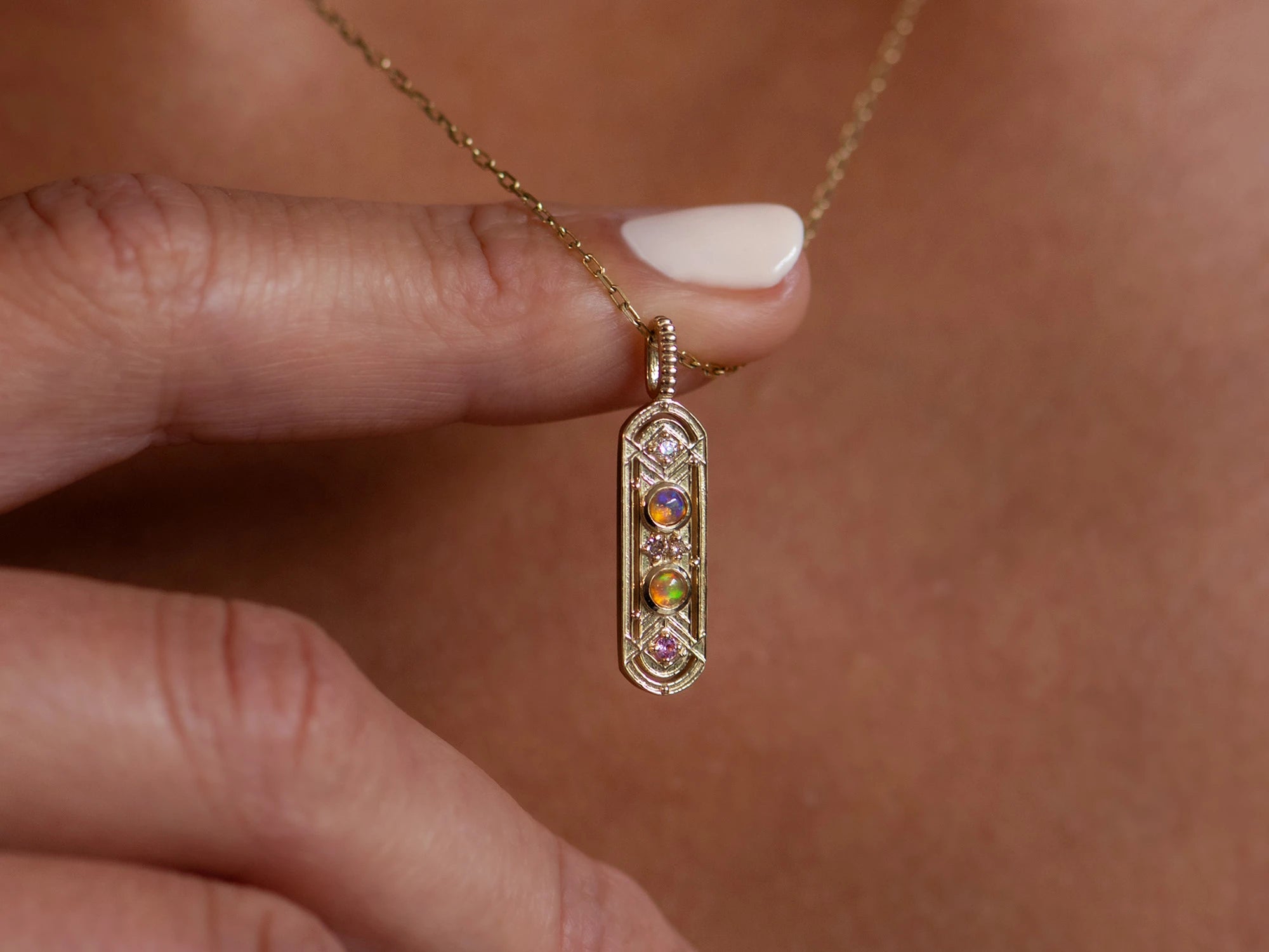 Zoomed in shot of women wearing a long, gold oval necklace with two circular opals. She is holding it away from her chest with one finger.