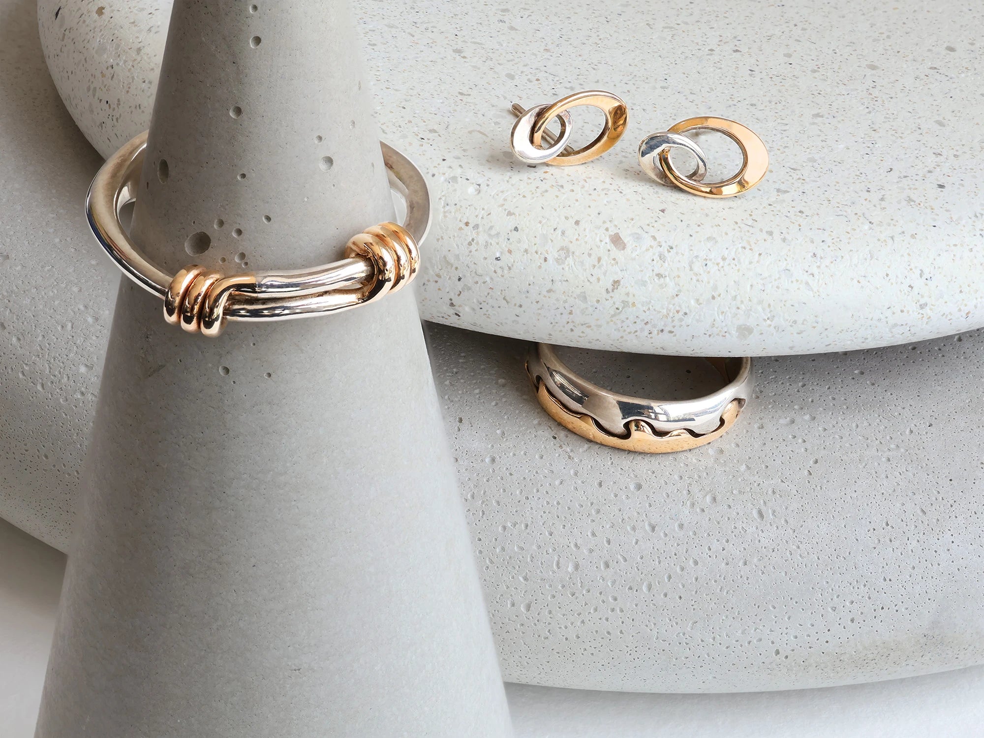 Two silver and gold rings with silver and gold oval earrings set on grey stones.