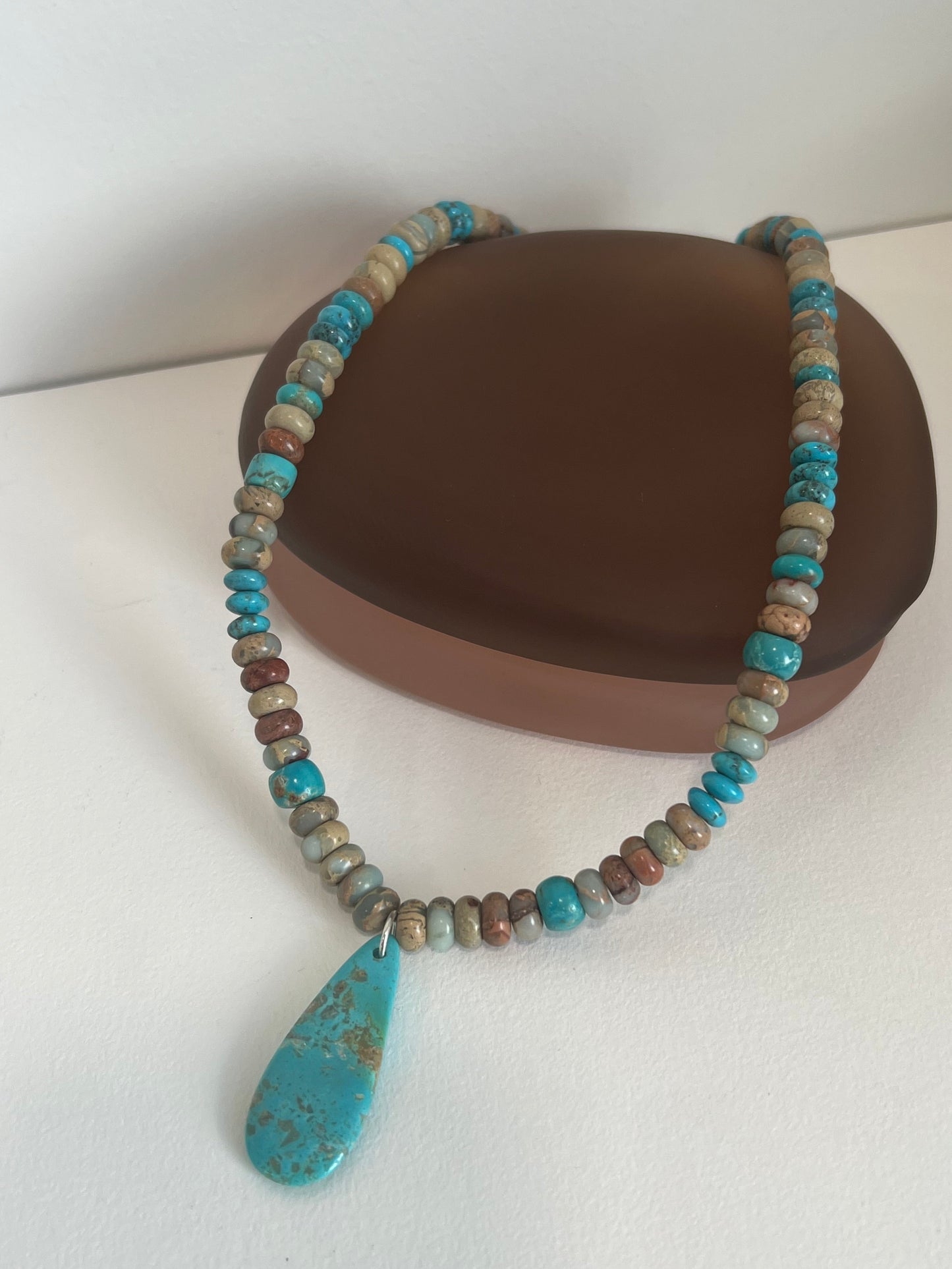 Beaded necklace with a large turquoise stone pendant on a white surface