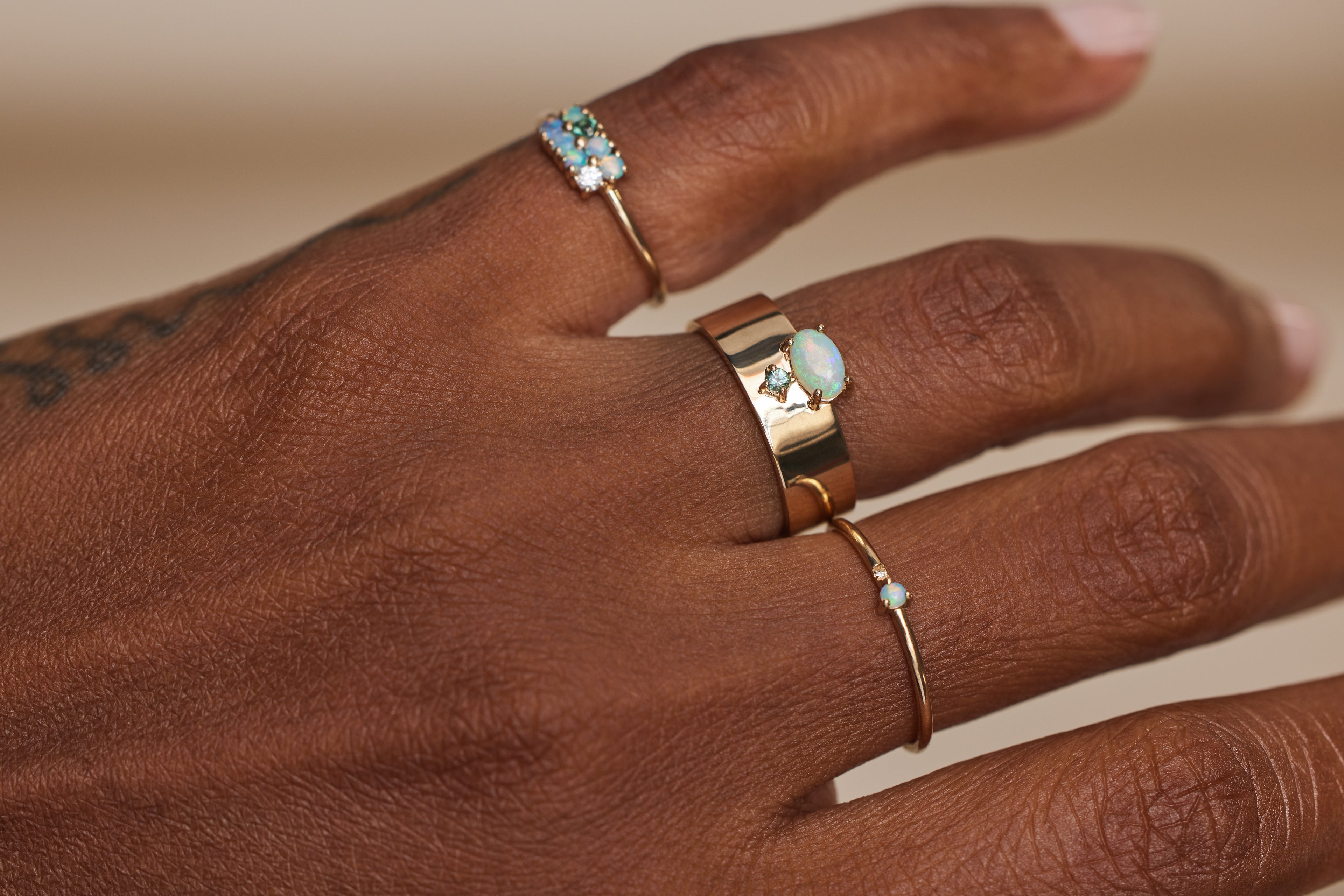 Woman's hand with an opal rings on 3 fingers. There's two thin gold bands and one thicker gold band.