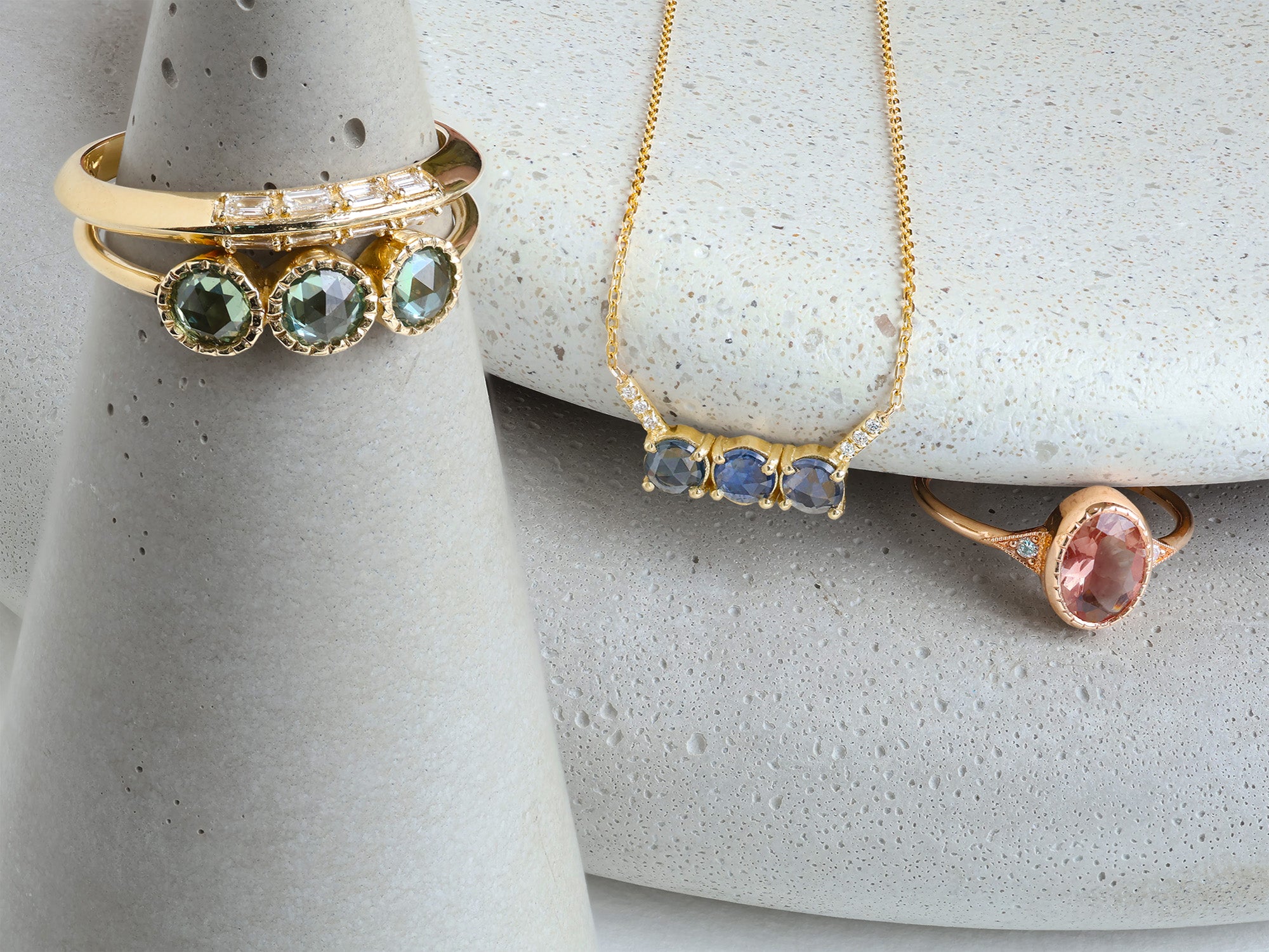 Gold jewelry with a a mixture of colored stones displayed on grey stones.