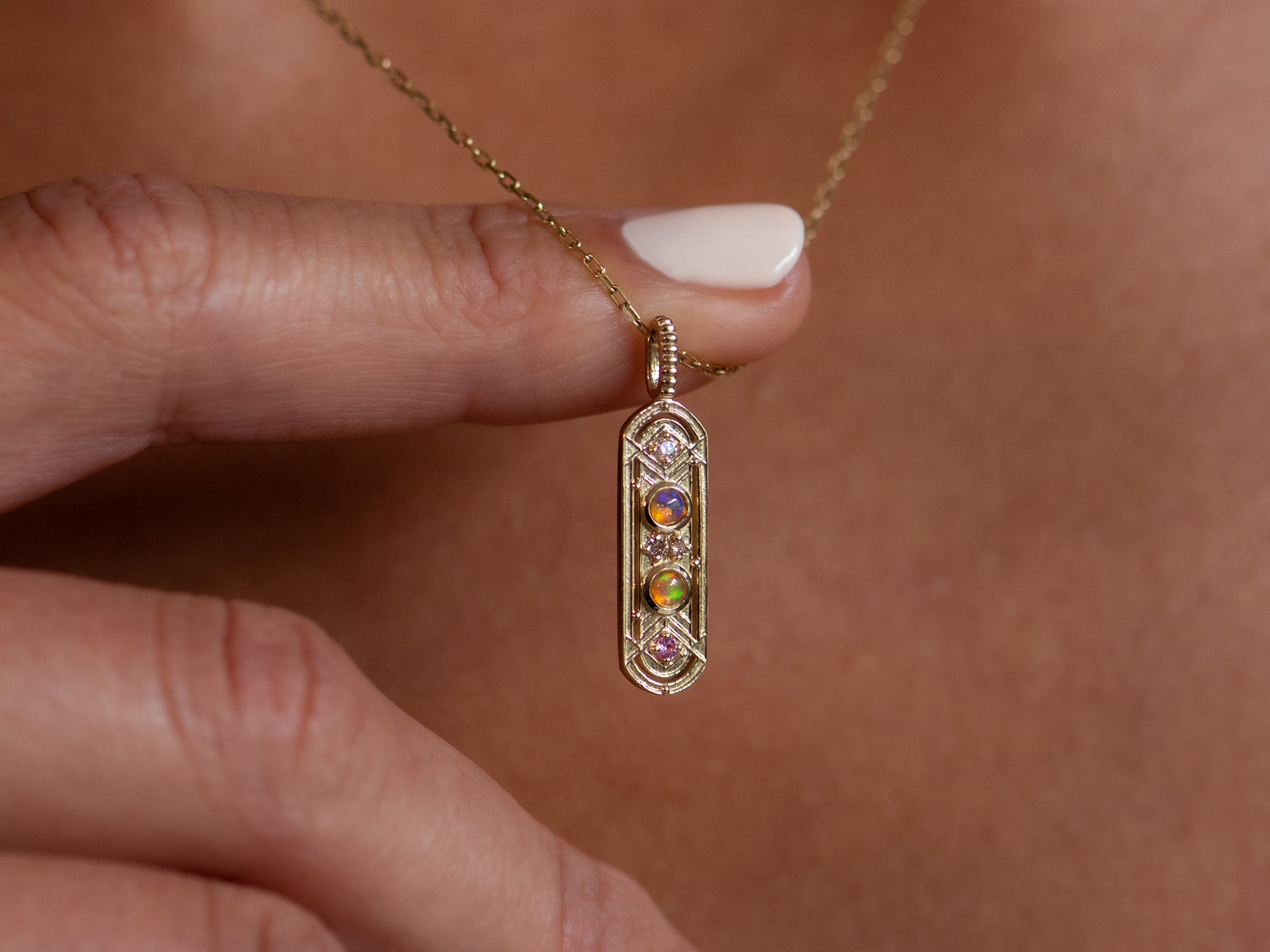 Zoomed in shot of women wearing a long, gold oval necklace with two circular opals.  She is holding it away from her chest with one finger.