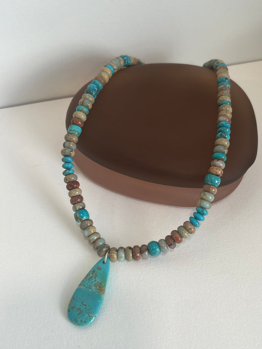 Beaded necklace with a large turquoise stone pendant on a white surface