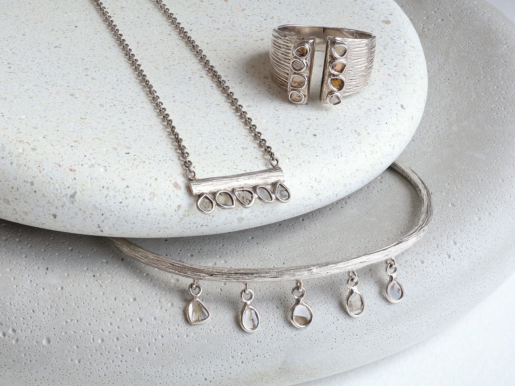 Sterling silver and sliced diamond necklace, ring, and bracelet set on grey stones.