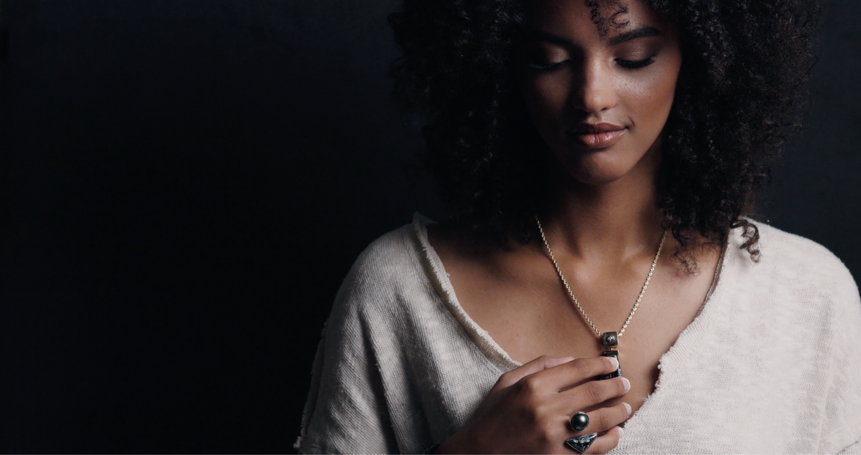 Woman wearing a pearl and opal ring holding a necklace and looking down.